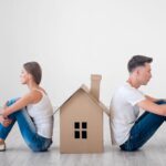 Couple sitting on opposite sides of a small cardboard house - legal separation in Ontario - Kelly Jordan Family Law.