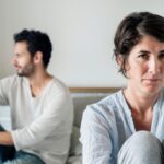 Unhappy woman and man sitting on a bed, with woman looking forward - how to prepare when telling your spouse you want a divorce - insights from Kelly Jordan Family Law.